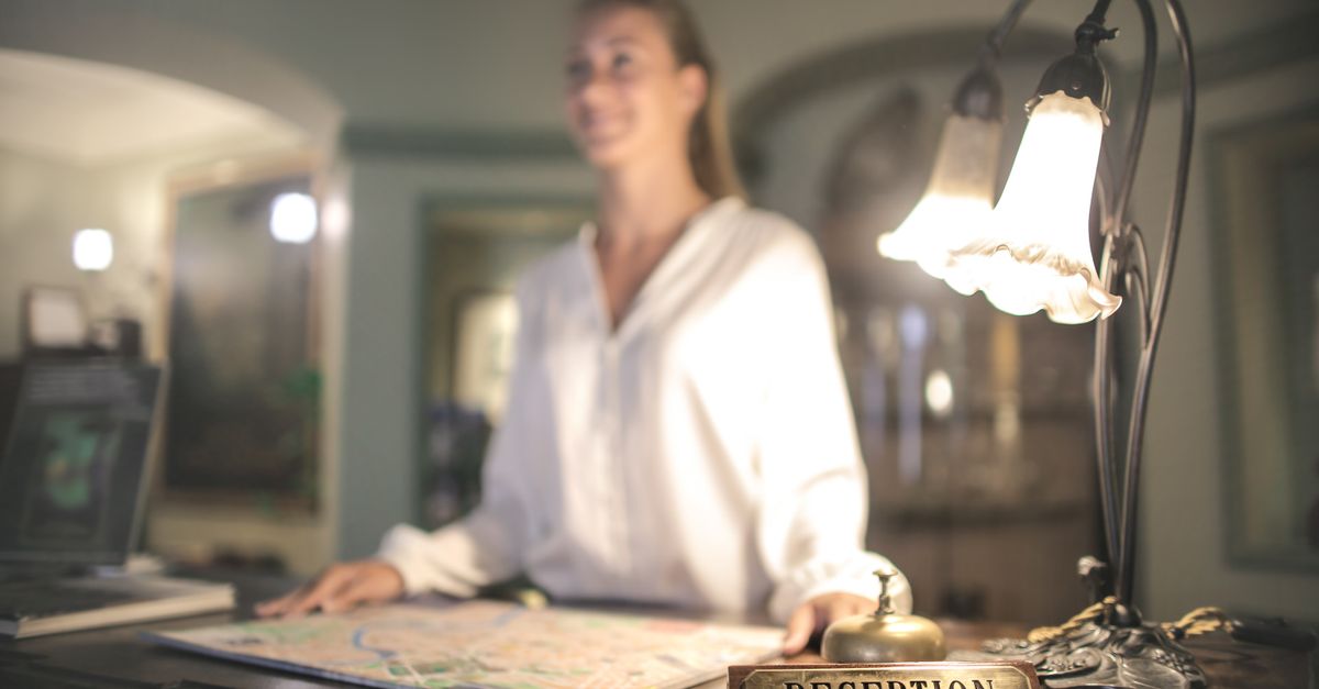 Blurred female in white shirt standing at reception desk with map on table and smiling while looking away
