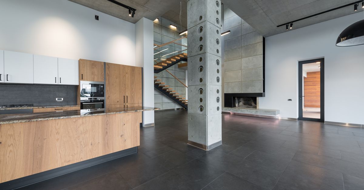 Spacious lobby with marching stairs and wooden kitchen furniture in corner near column