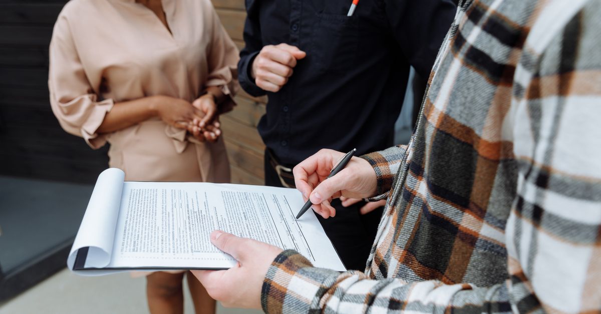Three adults in an office setting discussing and signing a document.