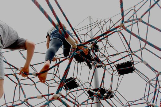 Kids enjoying a playful climb on a geometric rope structure outdoors.