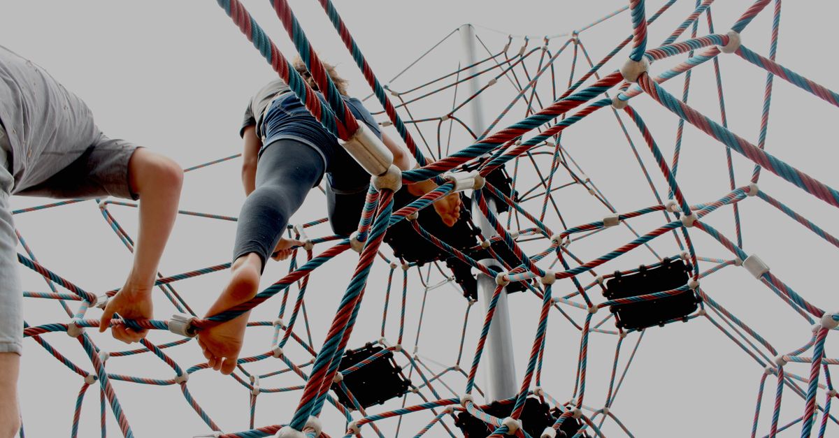 Kids enjoying a playful climb on a geometric rope structure outdoors.