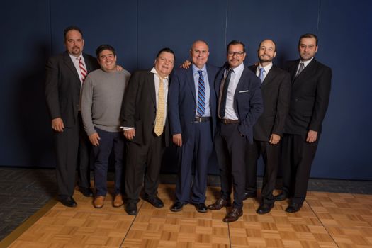 A group of men in suits posing and smiling together at an indoor social gathering.