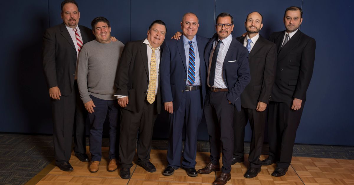 A group of men in suits posing and smiling together at an indoor social gathering.