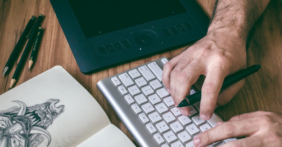A designer's hands working on digital art with a tablet, keyboard, and sketchbook.