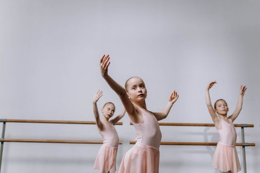 Three young ballerinas in pink tutus practice in a ballet studio, showcasing graceful choreography.
