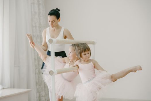 Ballet class with young girls in tutus practicing at the barre, guided by their teacher.