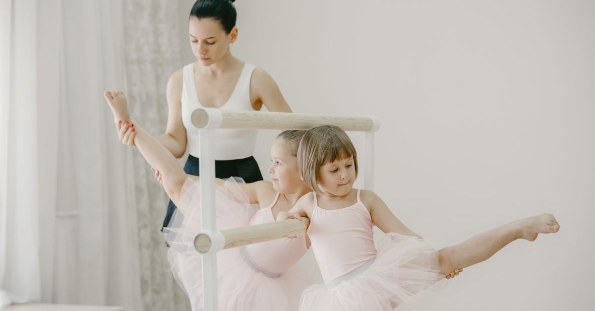 Ballet class with young girls in tutus practicing at the barre, guided by their teacher.