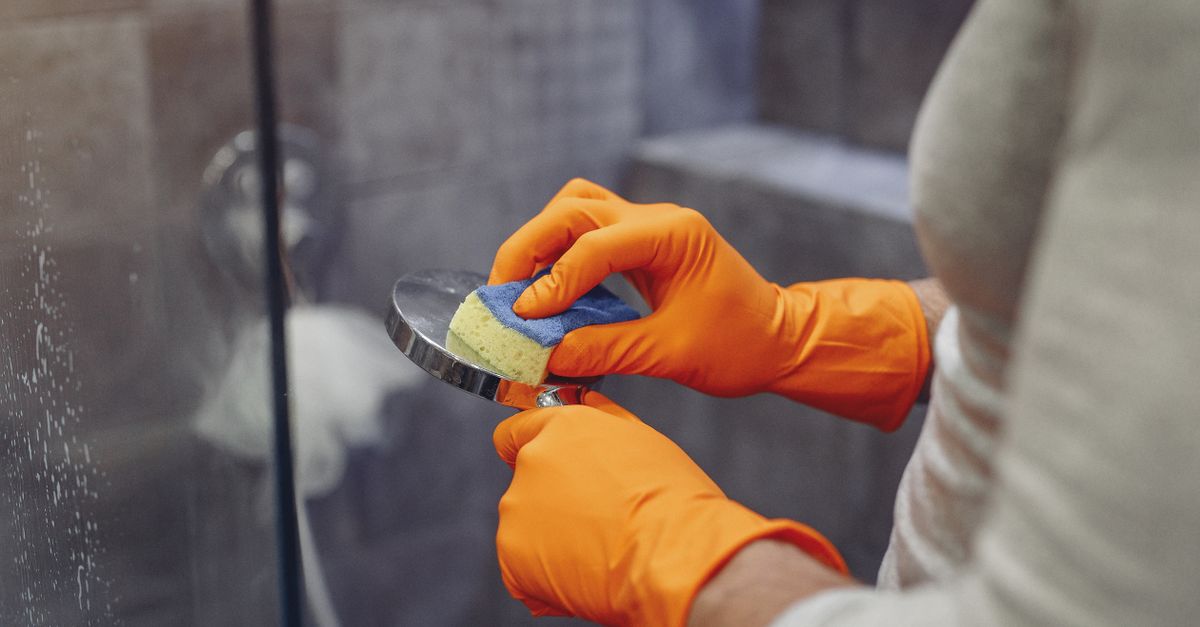 Crop faceless male in orange rubber gloves wiping by sponge shower nozzle