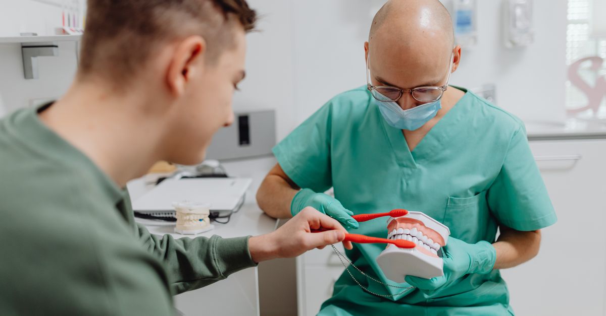 Dentist demonstrating proper brushing technique to patient using dental model.