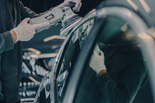 Close-up of car detailing process with polishing machine and reflective surface in workshop.