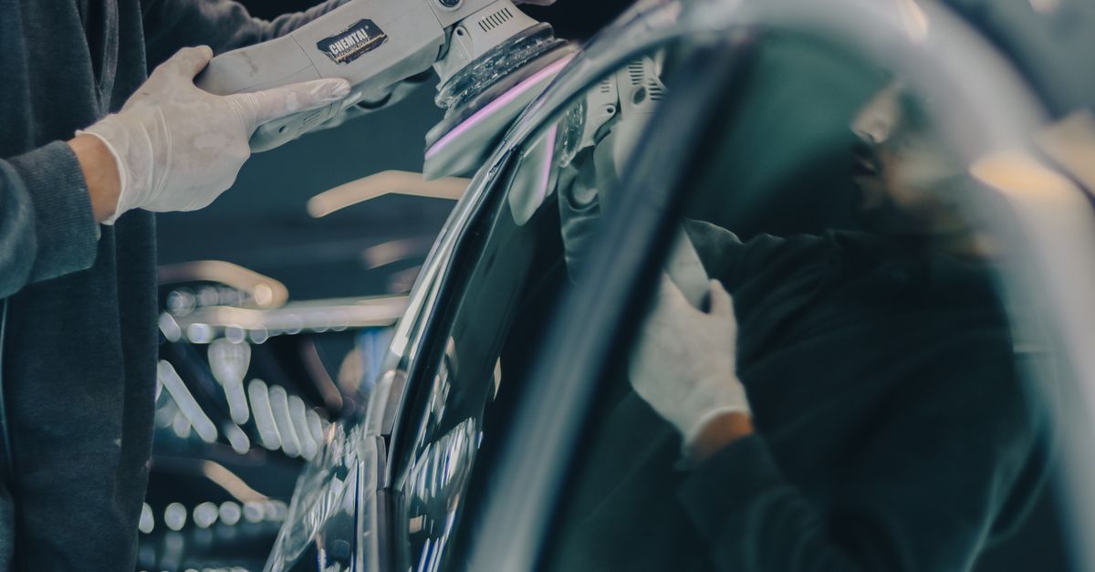 Close-up of car detailing process with polishing machine and reflective surface in workshop.