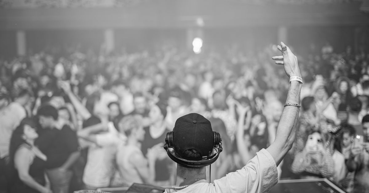 DJ in control, hyping up a large crowd at a lively nightclub event, creating an electrifying atmosphere.