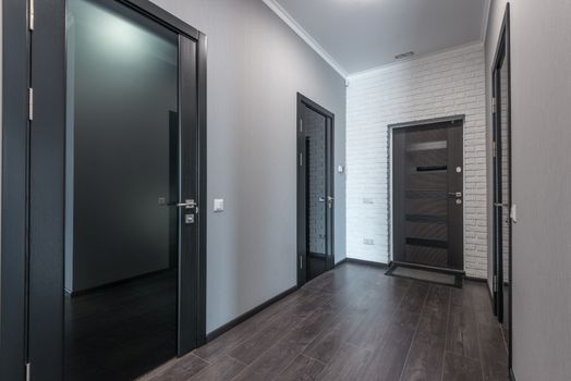 Interior of empty spacious corridor with laminate floor and black doors with glass parts and white ceiling and gray painted walls