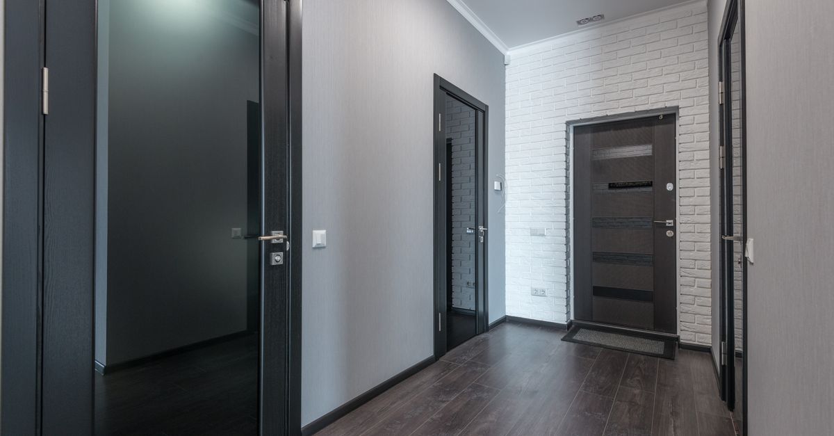 Interior of empty spacious corridor with laminate floor and black doors with glass parts and white ceiling and gray painted walls