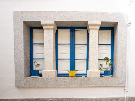 A bright blue window with stone framing, featuring vibrant potted plants.
