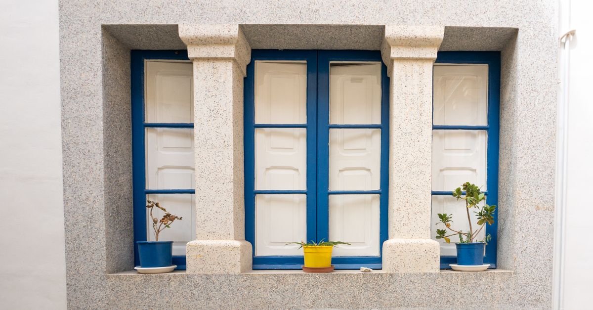 A bright blue window with stone framing, featuring vibrant potted plants.