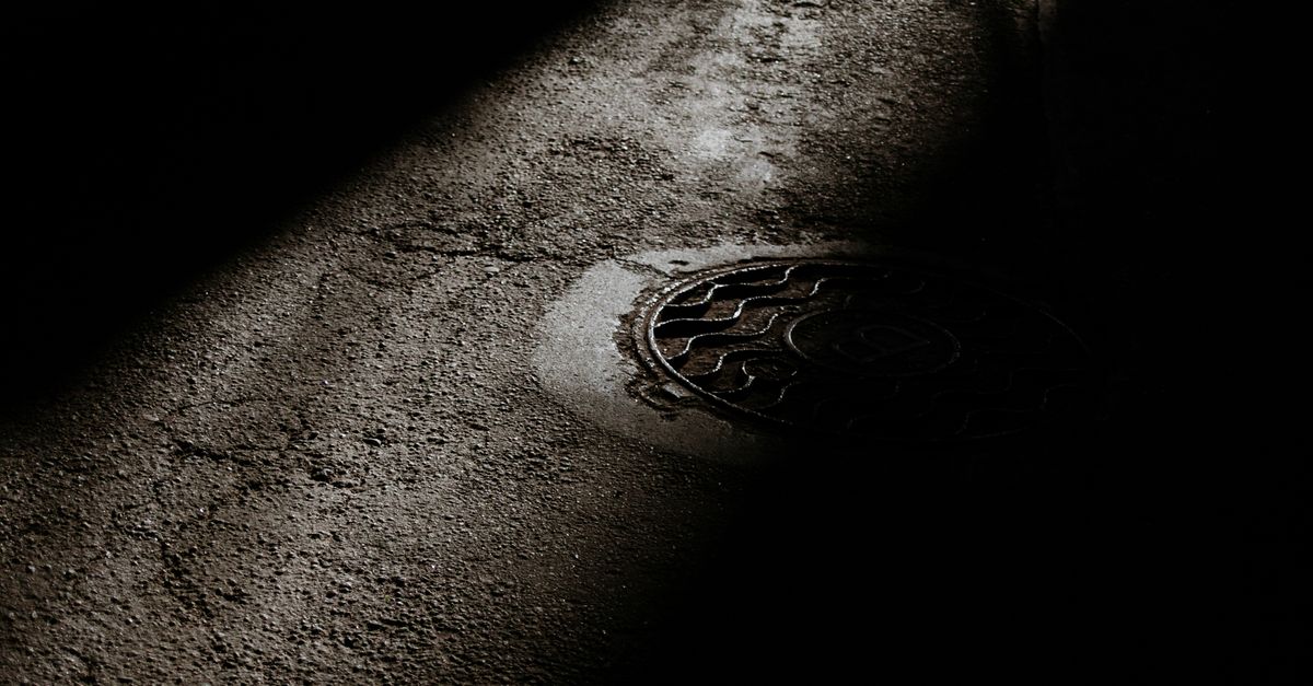From above of manhole with metal cover on rough asphalt road at night