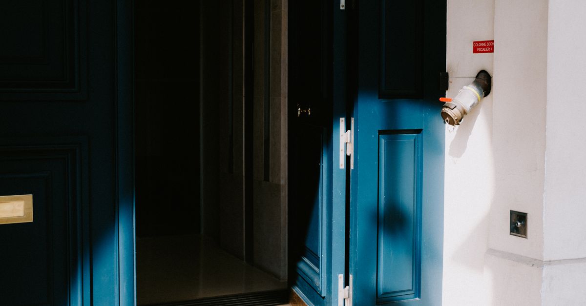 A sunlit blue door slightly ajar in a residential building entrance, casting shadows.