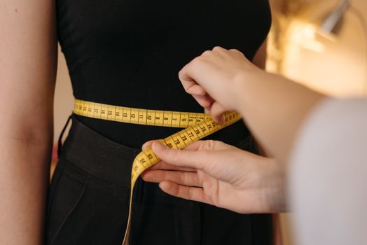 Close-up of tailor's hands measuring a person's waist with a yellow tape.