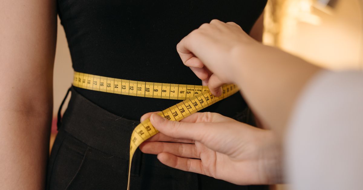 Close-up of tailor's hands measuring a person's waist with a yellow tape.