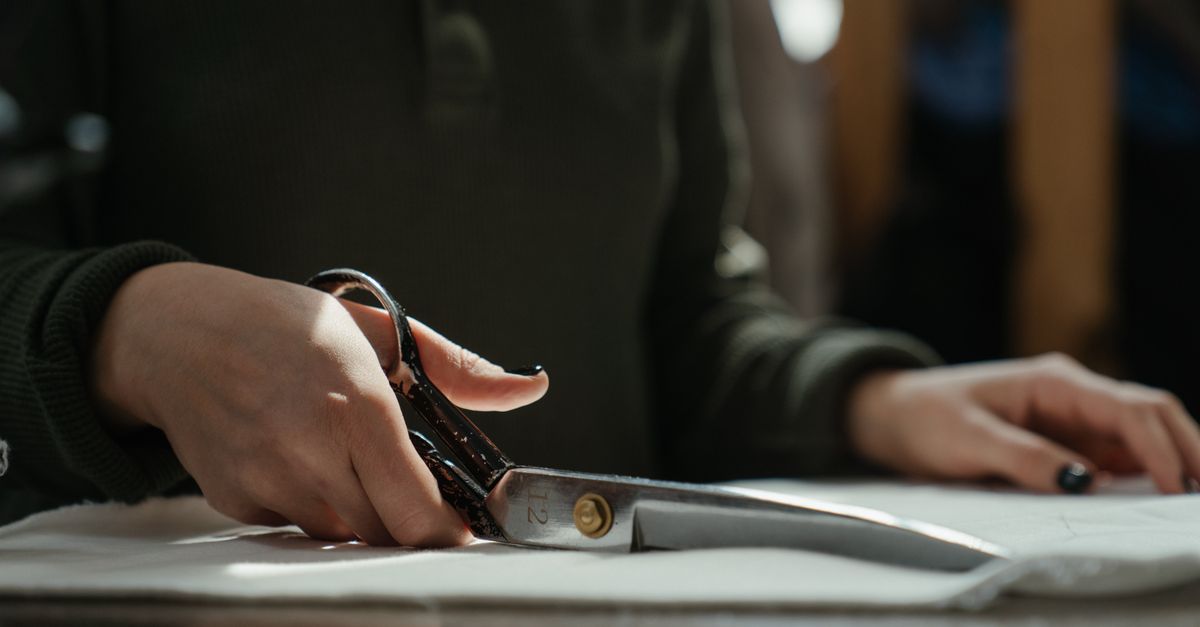 Close-up of a tailor's hands cutting fabric with scissors, emphasizing craftsmanship and skill.