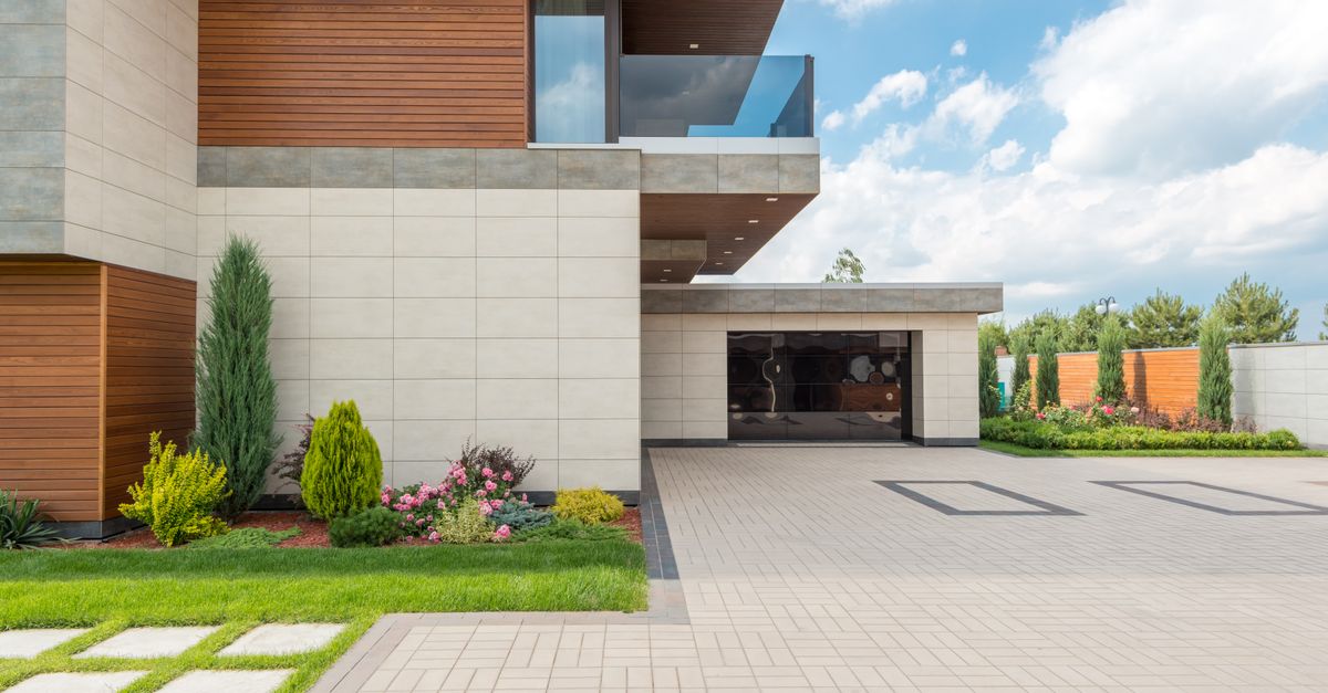 A modern minimalist house with a spacious driveway, landscaped garden, and clear blue sky.
