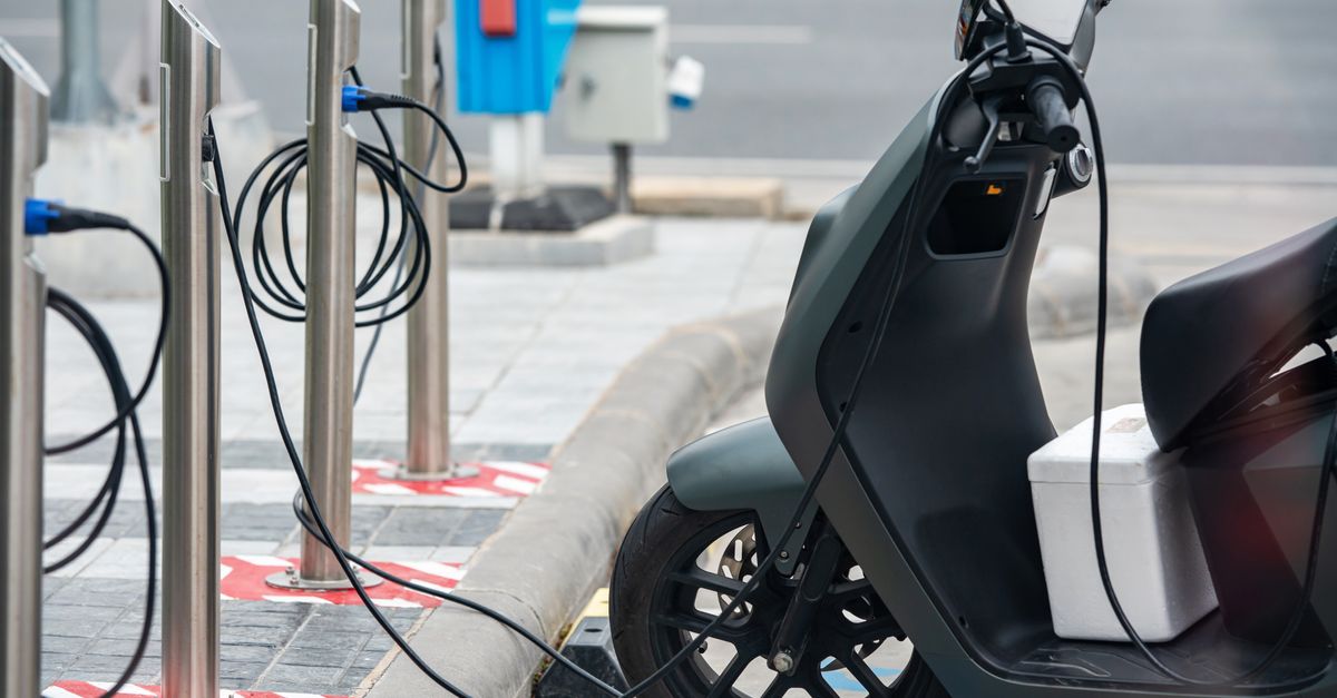 Electric scooter plugged into a charging station in a city environment, showcasing eco-friendly urban transportation.