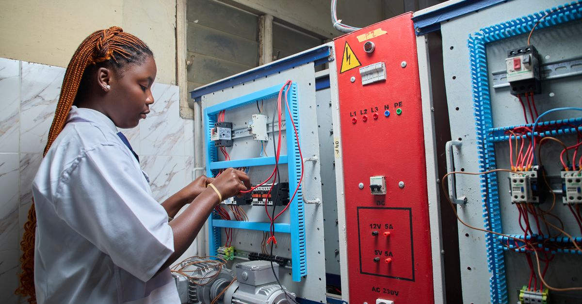 Young female technician repairing electrical control panel in industrial setting.