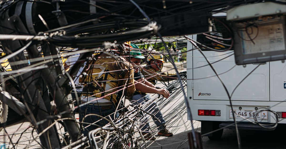 Workers managing tangled power lines by a street setup near a vehicle, highlighting infrastructure challenges.