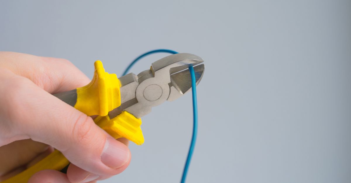 Detailed image of a hand using pliers to cut a blue wire on a gray background.