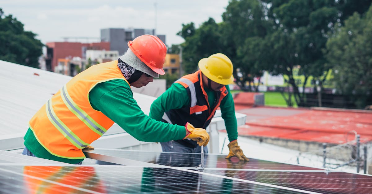 Two workers installing rooftop solar panels safely equipped with PPE and tools.