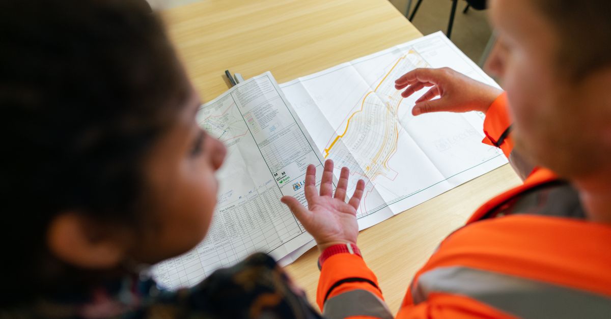 Two engineers reviewing construction blueprints on a table in an office setting.