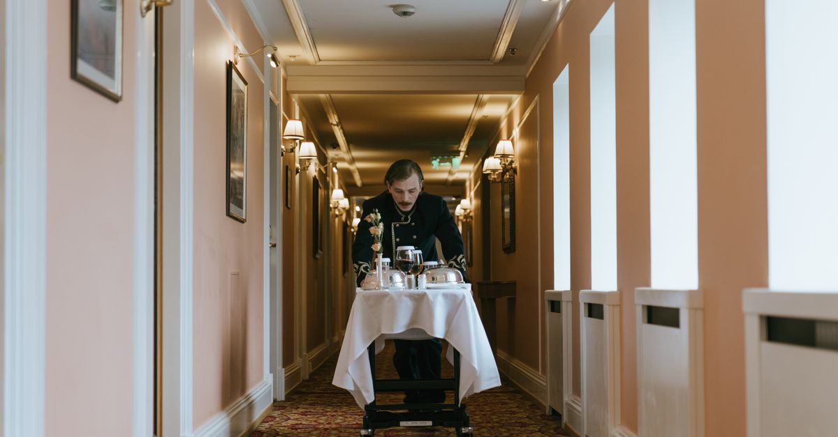A hotel staff member pushes a room service trolley in a luxurious corridor.