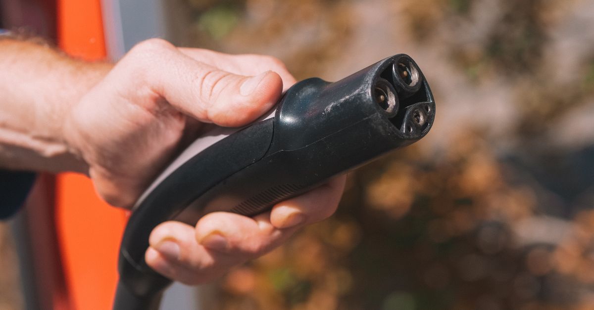 Hand holding an electric vehicle charging plug, symbolizing clean energy and innovation.