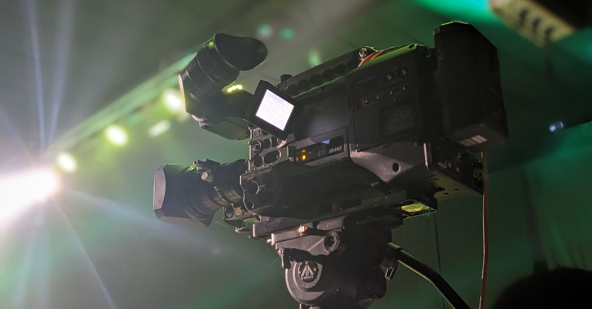 Close-up of a professional video camera capturing an event, highlighting its features under stage lighting.