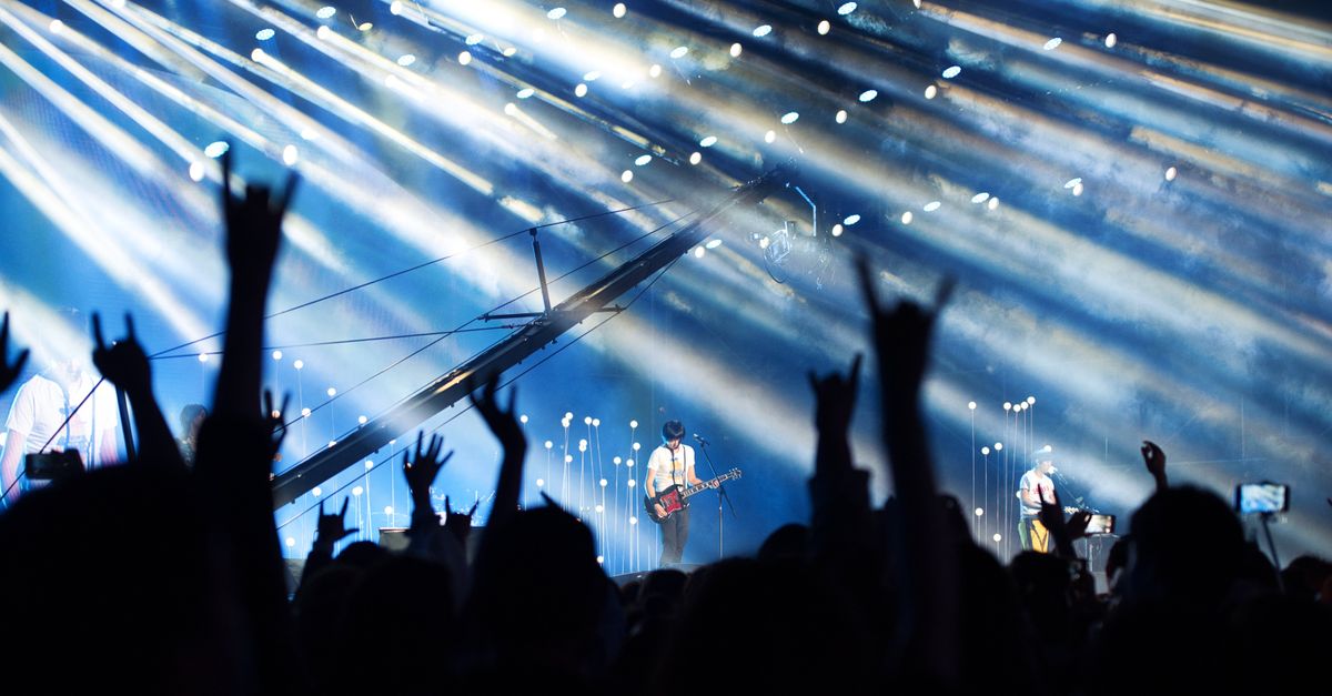 Energetic live music performance with crowd cheering under dramatic lighting.