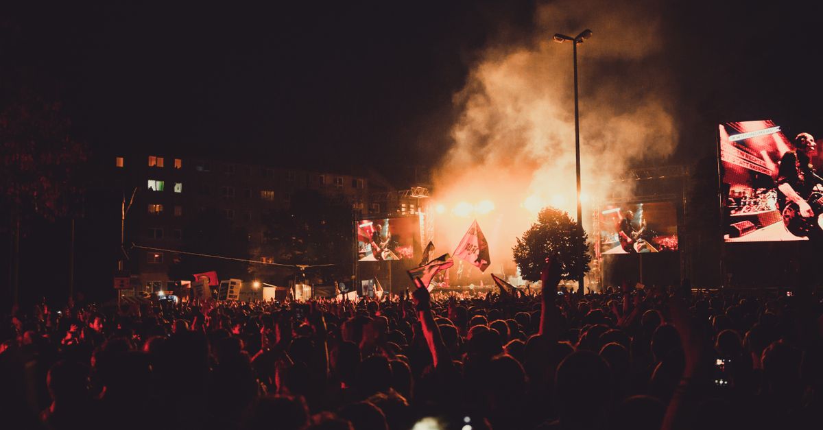 A dynamic live music concert with a large crowd, stage lights, and performer spotlight.
