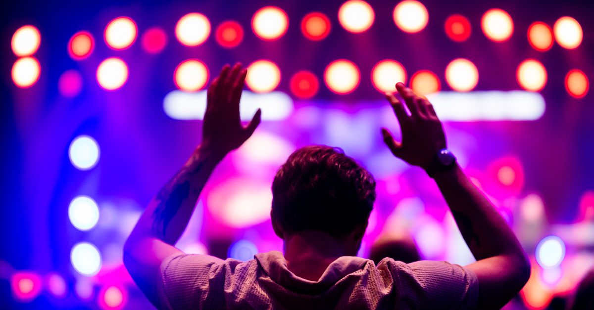 A lively concert atmosphere with colorful stage lights and an engaged audience member in silhouette.