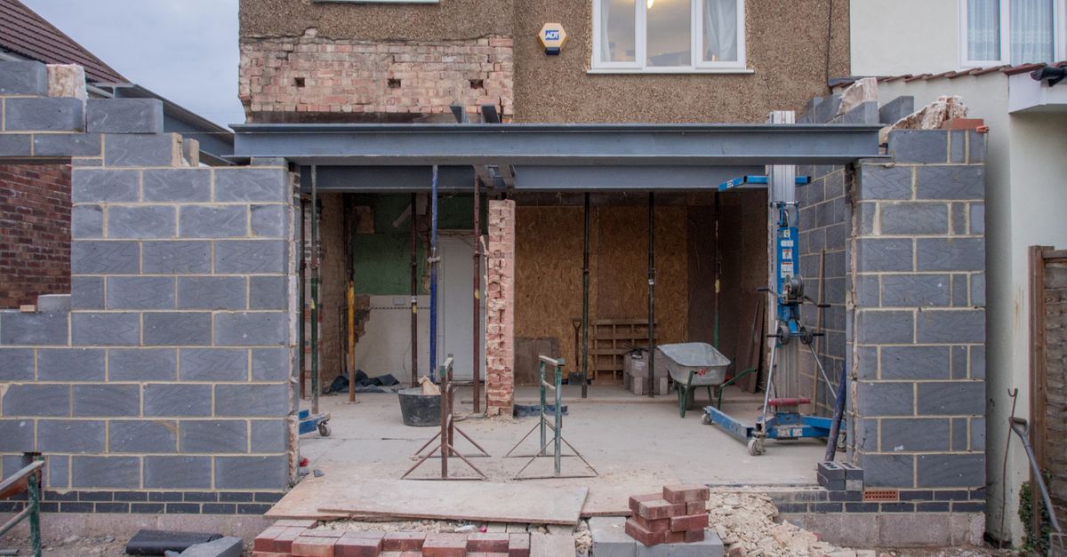 Brick house under renovation with an extension in progress. Visible construction site materials and structure.