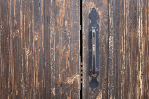 Closeup of weathered old rusty brown locked wooden door with cracks on surface with aged metal handle
