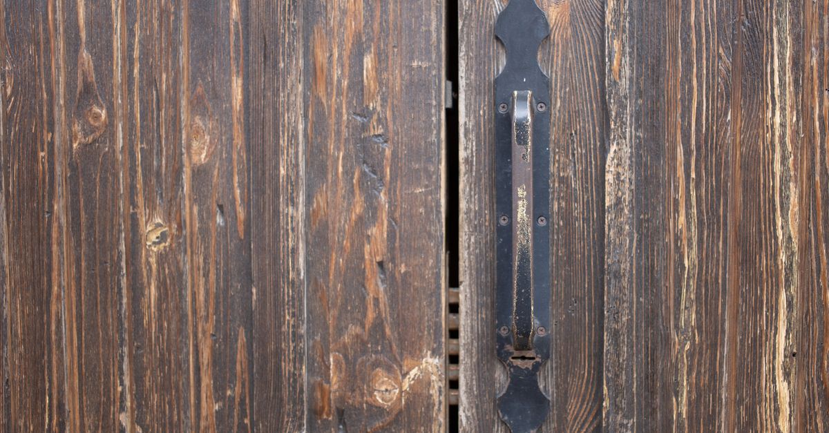 Closeup of weathered old rusty brown locked wooden door with cracks on surface with aged metal handle