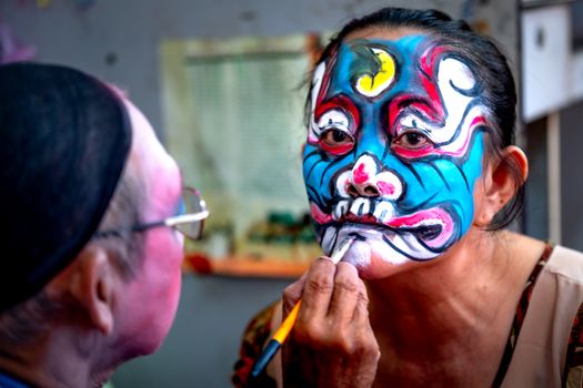 Colorful face painting in progress at a lively cultural festival indoors.