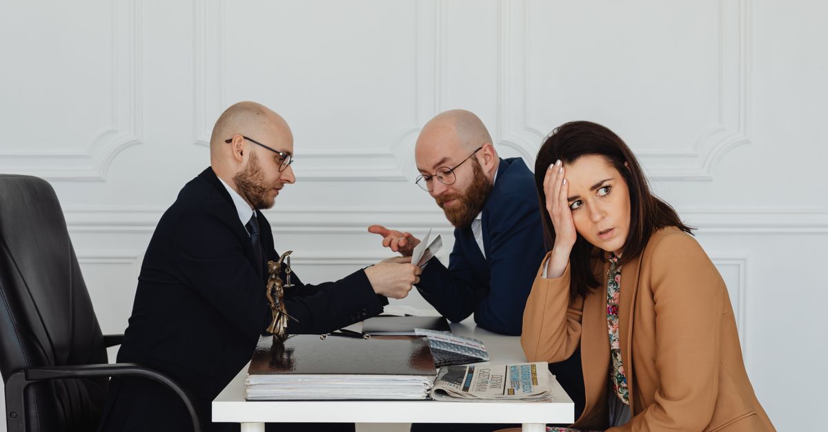 Two lawyers discuss documents with a worried client in a professional office setting.