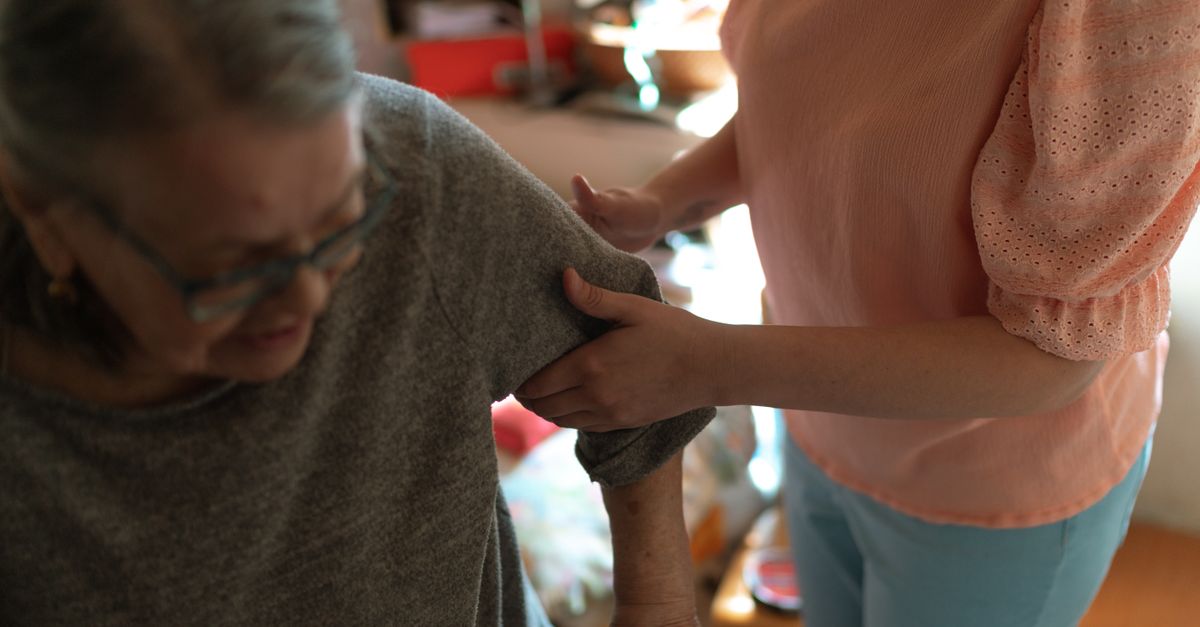 Compassionate caregiver helps elderly woman with mobility at home, offering caring support.