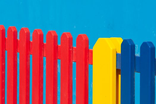 Vibrant red, yellow, and blue wooden fence panels against a clear blue backdrop.