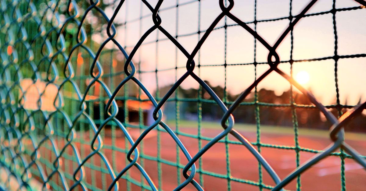 Close-up view of a chain link fence with a sunset over a sports field, creating a serene atmosphere.