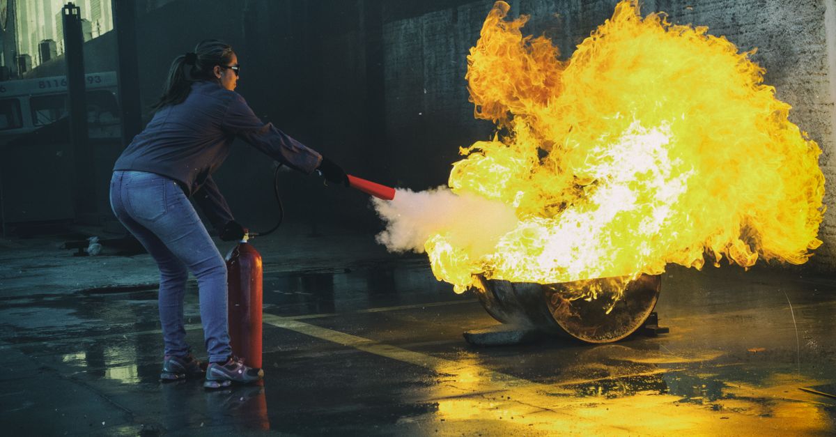 A woman uses a fire extinguisher to put out a large flame in an outdoor setting, showcasing fire safety.