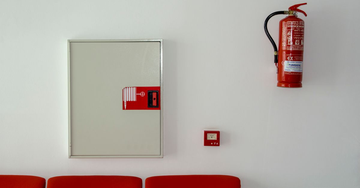 Fire extinguisher and safety equipment mounted on a white wall with red seating below.