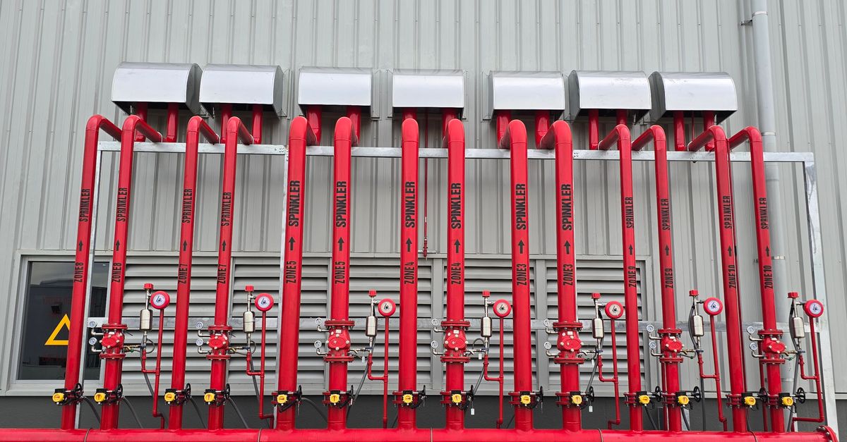 Red industrial fire sprinkler pipes aligned on a factory exterior wall.