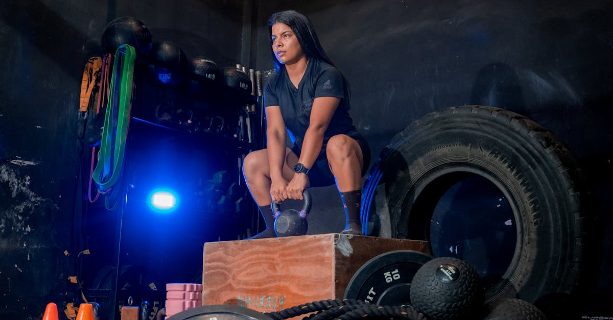 A woman squats with a kettlebell in a gym setting, focusing on strength training.